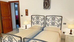 A bedroom with a double bed, two bedside tables with lamps, a wooden door, and a wall-mounted decoration.