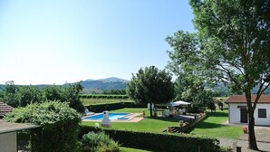 A pool with a pergola, a small garden, and a view of hills in the background.