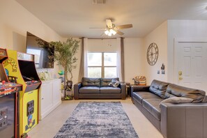 A living room with a sofa, a coffee table, a ceiling fan, a large window, and a wall clock. - Family Home w/ Community Perks in Peoria (Peoria)