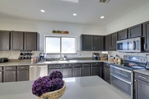 A modern kitchen with dark cabinets, stainless steel appliances, and a central island with a purple flower arrangement. - Family Home w/ Community Perks in Peoria (Peoria)