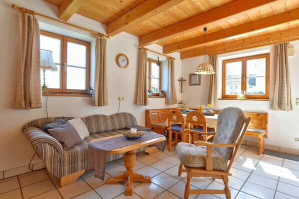 A cozy room with a wooden ceiling, a sofa, a dining table, and chairs.
