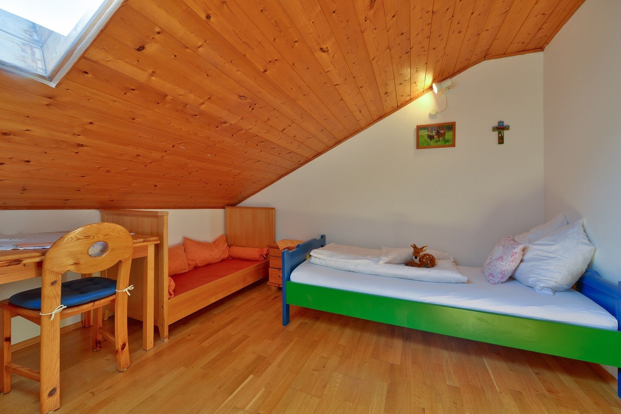 Una habitación tipo dormitorio con techo inclinado, mobiliario de madera, una cama, un escritorio y una silla.