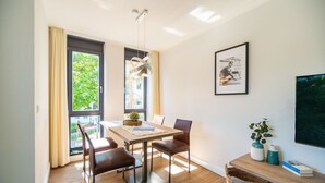 Uma área de refeições com mesa, cadeiras, luminária pendente, quadro e janela com cortinas.
