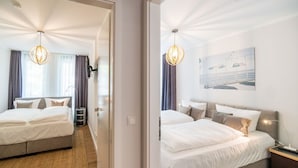 Quarto de hotel com cama, mesa de cabeceira, luminária, quadro na parede e janela com cortinas.