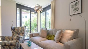 Ein Wohnzimmer mit Sofa, Sessel und Couchtisch, großen Fenstern mit Blick und einer Pendelleuchte.