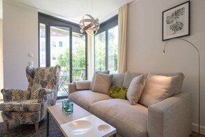 A living room with a sofa, armchair, and coffee table, large windows with a view, and a pendant light. - Villa Maxim, App. 1, Germany (Heringsdorf)