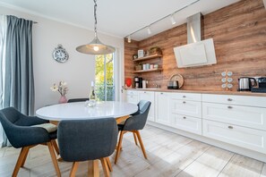 Une cuisine moderne avec des meubles blancs, des éléments décoratifs en bois et une table de salle à manger ronde, accompagnée de chaises.