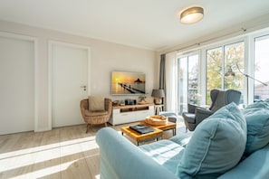 Ein modernes Wohnzimmer mit einer Couch, einem Couchtisch, einem Korbstuhl und einem an der Wand montierten Fernseher.