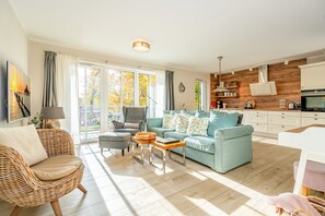 Ein großzügiges Wohnzimmer mit großem Fenster, einer Couch, einem Sessel und einem Couchtisch.