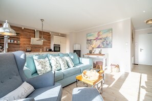 Un salon moderne avec un canapé bleu clair, un mur d’accent en bois et une cuisine en arrière-plan.