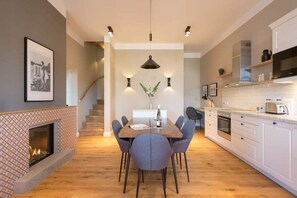 Una cocina moderna con armarios blancos, horno empotrado y microondas. Hay una mesa de comedor con sillas y una lámpara colgante.