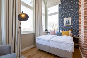Un dormitorio con una cama, una lámpara, una ventana y una pared con estampado floral.