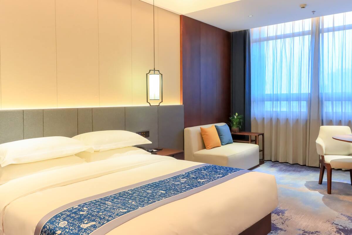 A hotel room with a large bed, a sofa, a small table, and a chair.