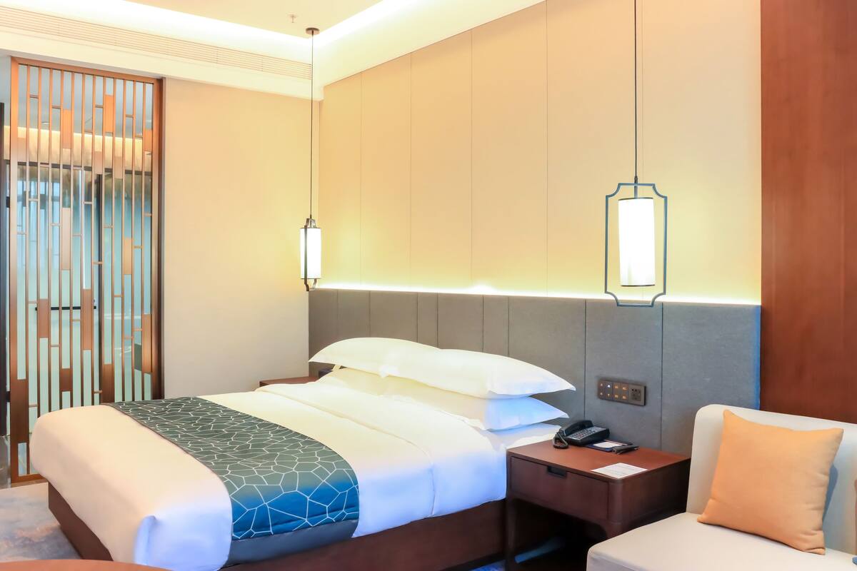 A hotel room with a bed, bedside table, and a chair.