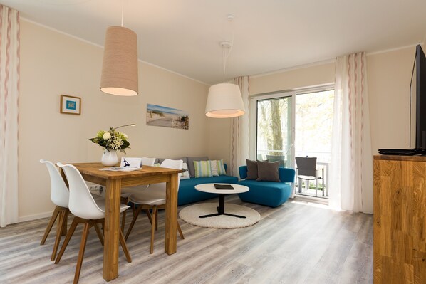 Un salon moderne avec une table à manger en bois, des chaises blanches, un canapé bleu et une table basse ronde.