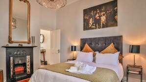 A hotel room with a large bed, a fireplace, a large mirror, and a painting on the wall. - Beaumont Cottages 2 by CTHA (Cape Town)