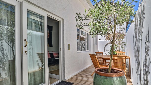 A covered patio with a wooden deck, a potted tree, and a dining area with wooden furniture. - Beaumont Cottages 2 by CTHA (Cape Town)