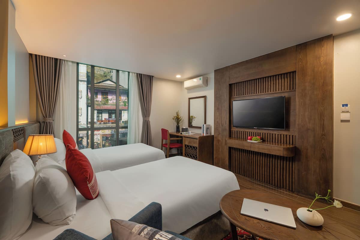 Una habitación de hotel con dos camas, un escritorio, un televisor y una ventana con cortinas.
