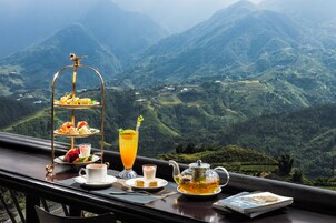 Una mesa con un juego de té, un vaso de zumo de naranja, una taza de café y una bandeja de pasteles, con vistas a la montaña.