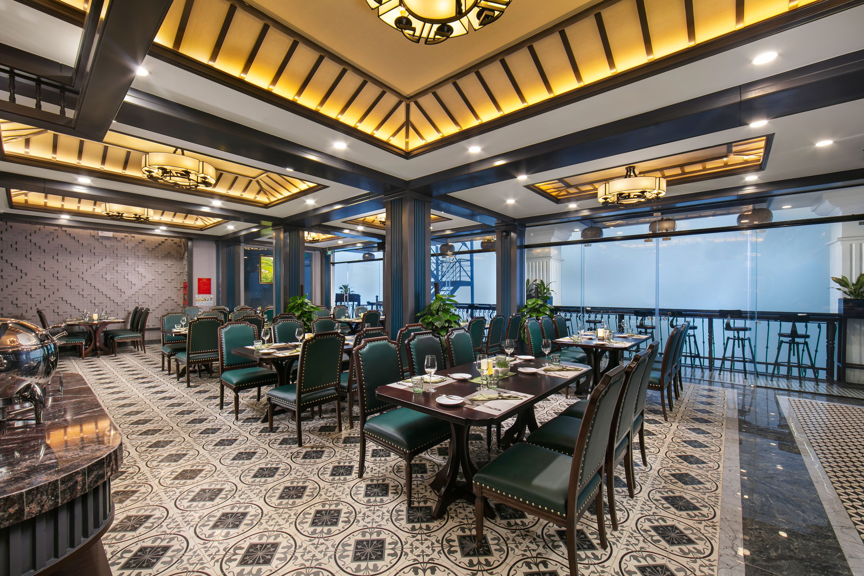 A restaurant with a patterned floor, green upholstered chairs, and a bar area.
