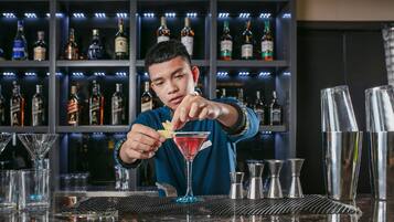 Un cantinero preparando un cóctel en un bar con estantes llenos de botellas de licor al fondo.