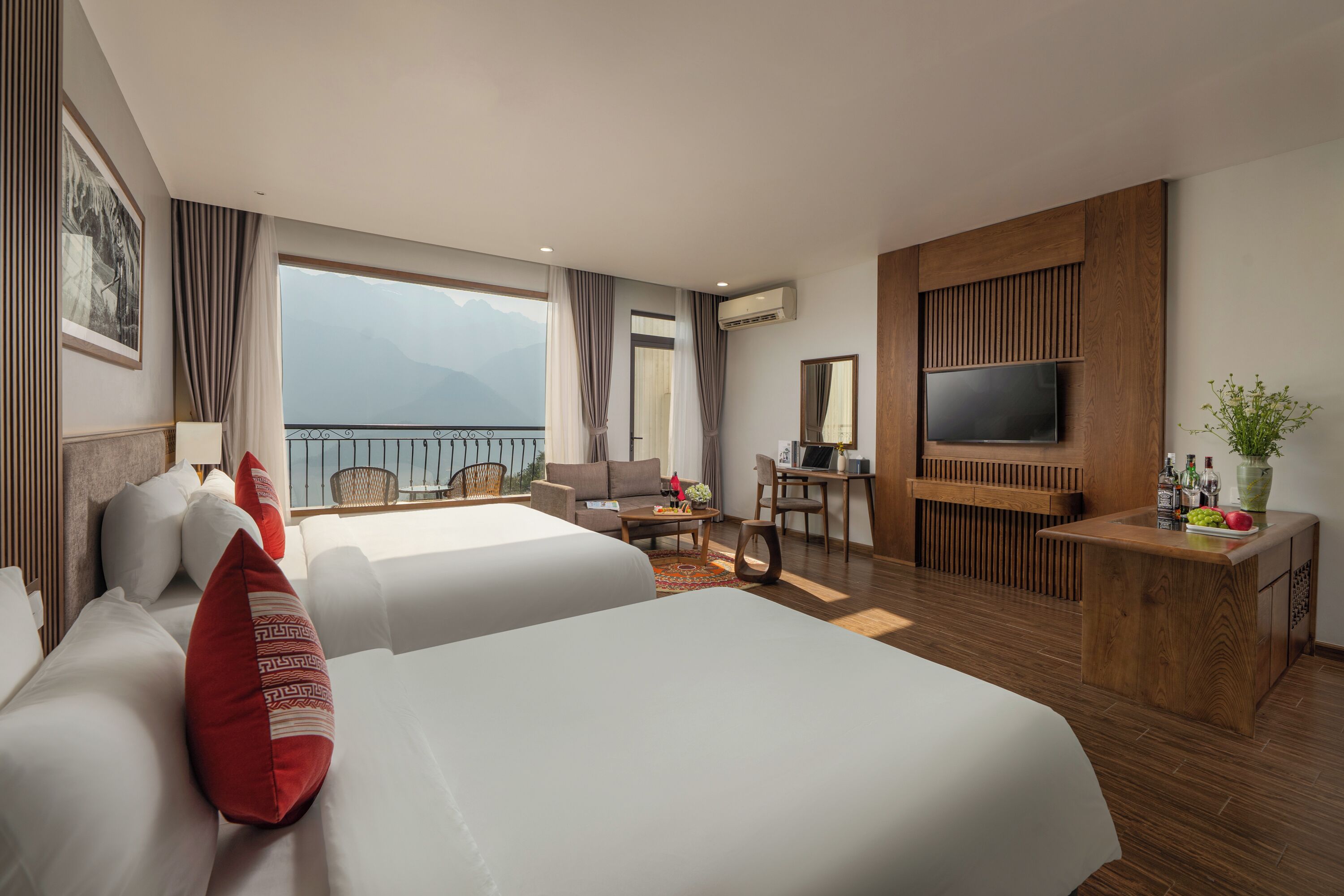Una habitación de hotel con dos camas, televisor, escritorio y balcón con vista a la montaña.