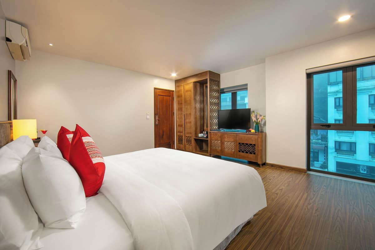Habitación de hotel con una cama grande, un armario de madera, un televisor de pantalla plana y un amplio ventanal con vistas a la ciudad.
