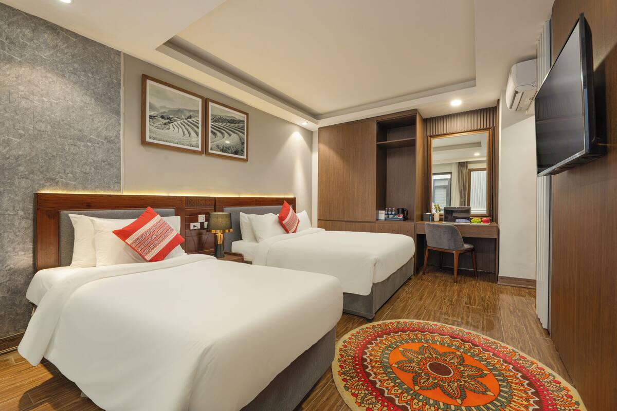 Habitación de hotel con dos camas, un escritorio, una silla, un televisor y un espejo grande.