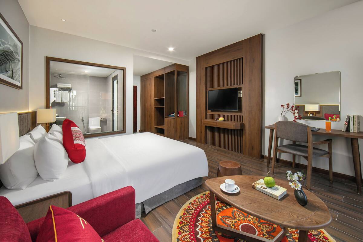 Una habitación de hotel con una cama grande, un escritorio con una silla, un televisor y un espejo.
