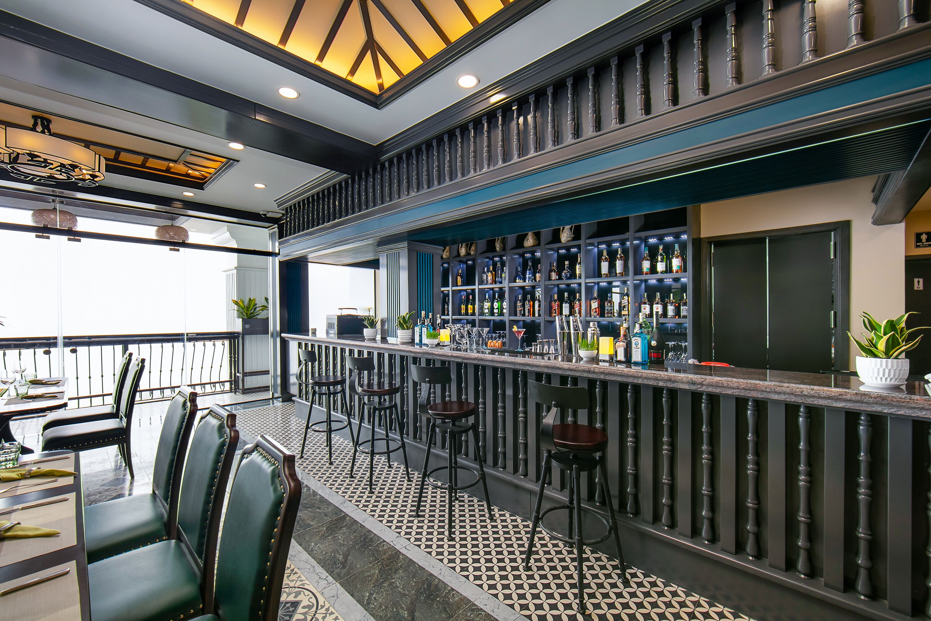 A bar area with a high ceiling, patterned floor, and bar stools.