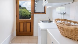 Eine kleine Küche mit Holztür, weißen Fliesen, einem Waschbecken und einem Korbwäscheschrank auf der Arbeitsplatte.