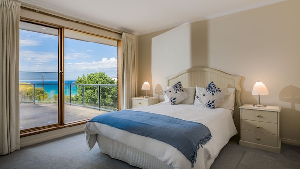 Ein Schlafzimmer mit einem großen Bett, zwei Nachttischen, Blick auf das Meer und einem Balkon.