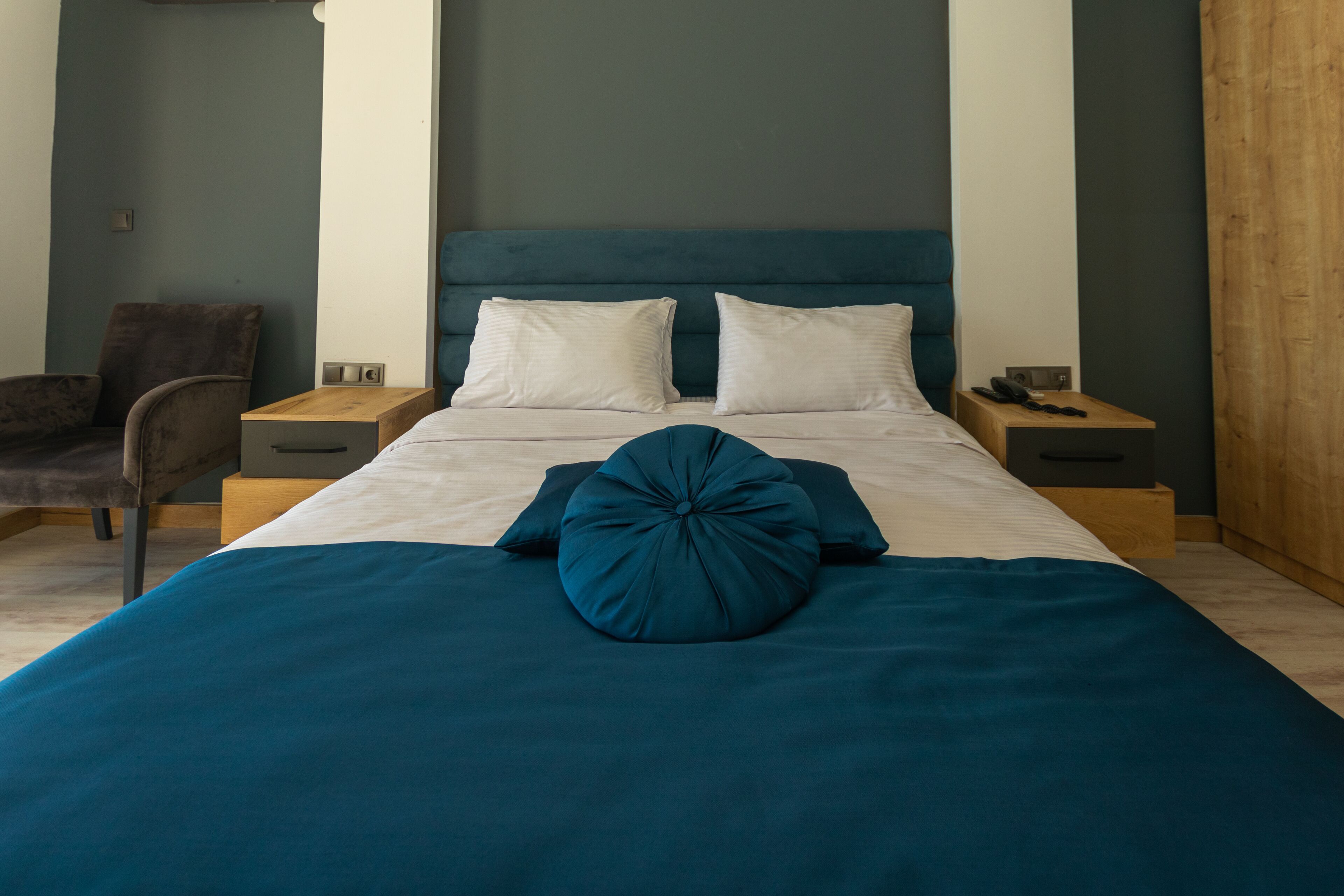 A neatly arranged bedroom with a bed, two pillows, a chair, and bedside tables.