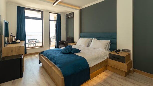 A modern hotel room with a large bed, a desk with a computer, a chair, and a view of the city. - Sunrise Hotel (Sinop)