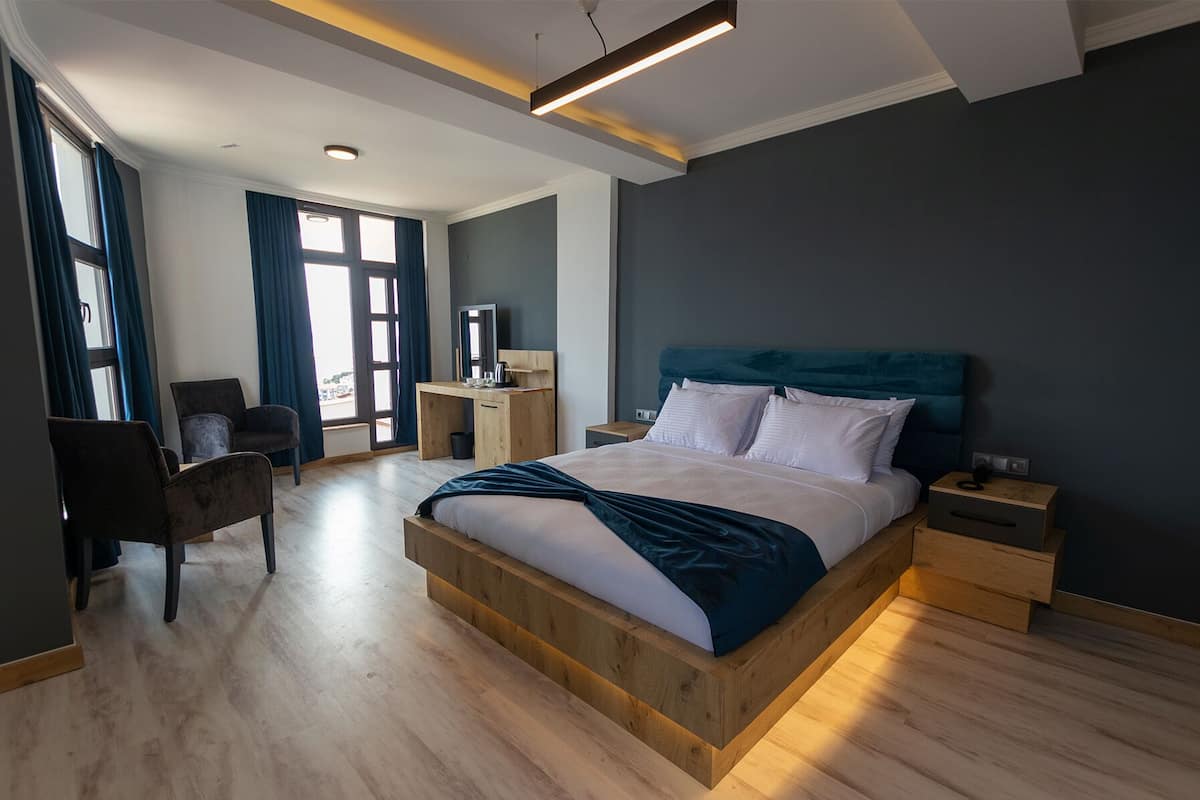 A modern hotel room with a large bed, wooden headboard, and a desk with a chair.