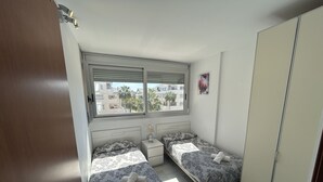 Quarto com duas camas, um guarda-roupa, uma janela e uma mesa de cabeceira.