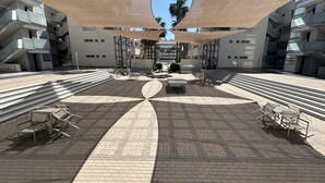 Amplo espaço ao ar livre com um conjunto de assentos no centro, rodeado por degraus e edifícios modernos.