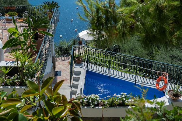 A pool area with a lifebuoy, potted plants, and a view of the sea.