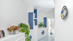 En hall med vita väggar, blå detaljer, en krukväxt, en vas med blommor och en dekorativ tallrik på väggen.
