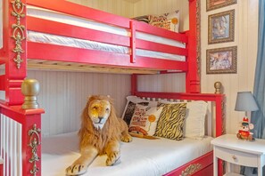 Habitación con literas, un león de peluche en la cama inferior, ropa de cama blanca y una mesita de noche con lámpara.