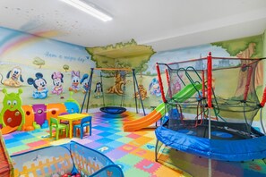 Una sala de juegos infantil con un trampolín, un corralito y piso de colores.