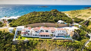A large, white, multi-story resort with a pool, surrounded by lush greenery and overlooking the ocean. - Villa Amalia – 6-Bedroom Luxury Oceanview Villa with Pool, Gym & Full Staff in St. Maarten (Philipsburg)