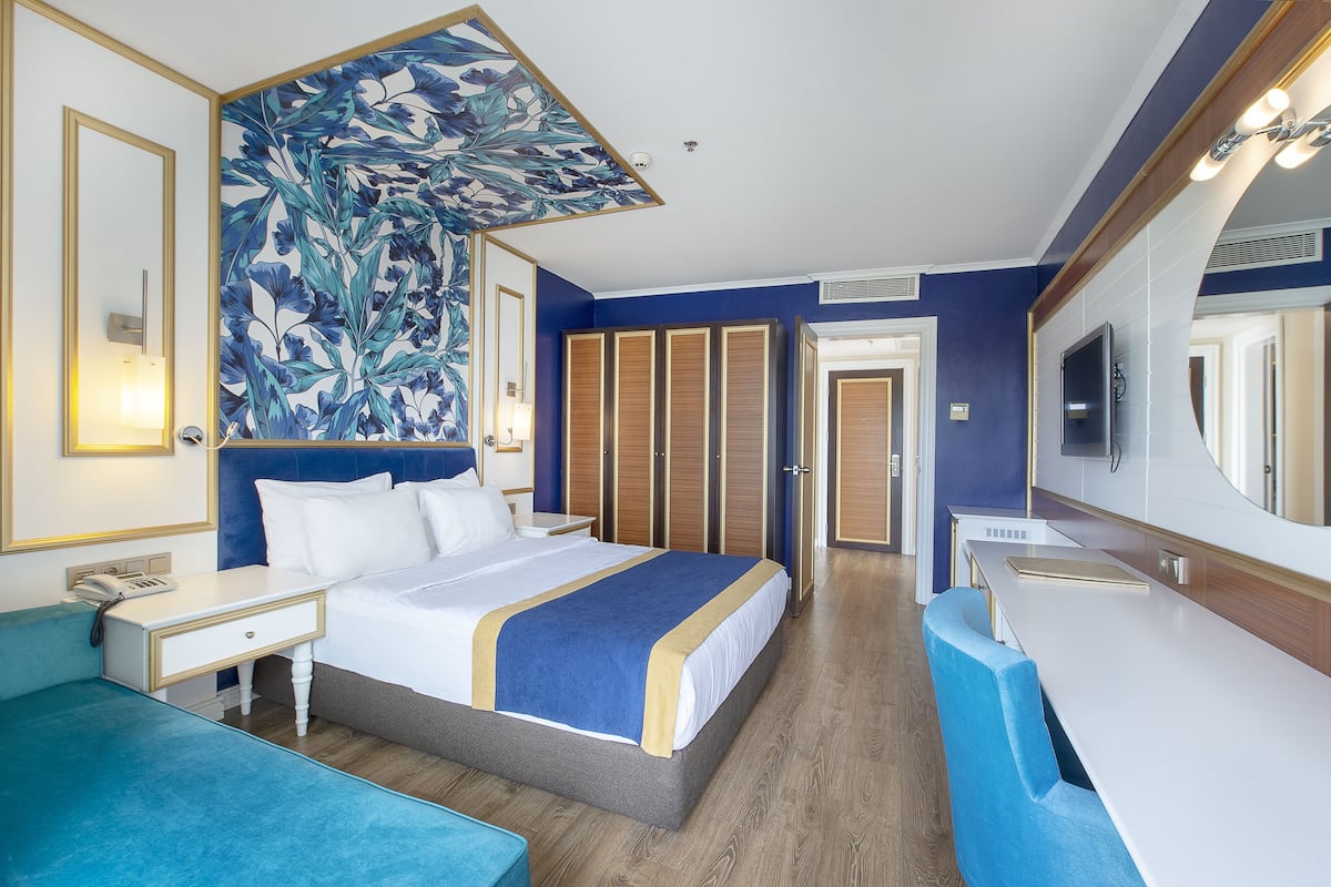A hotel room with a large bed, a desk, a chair, a mirror, and a television.