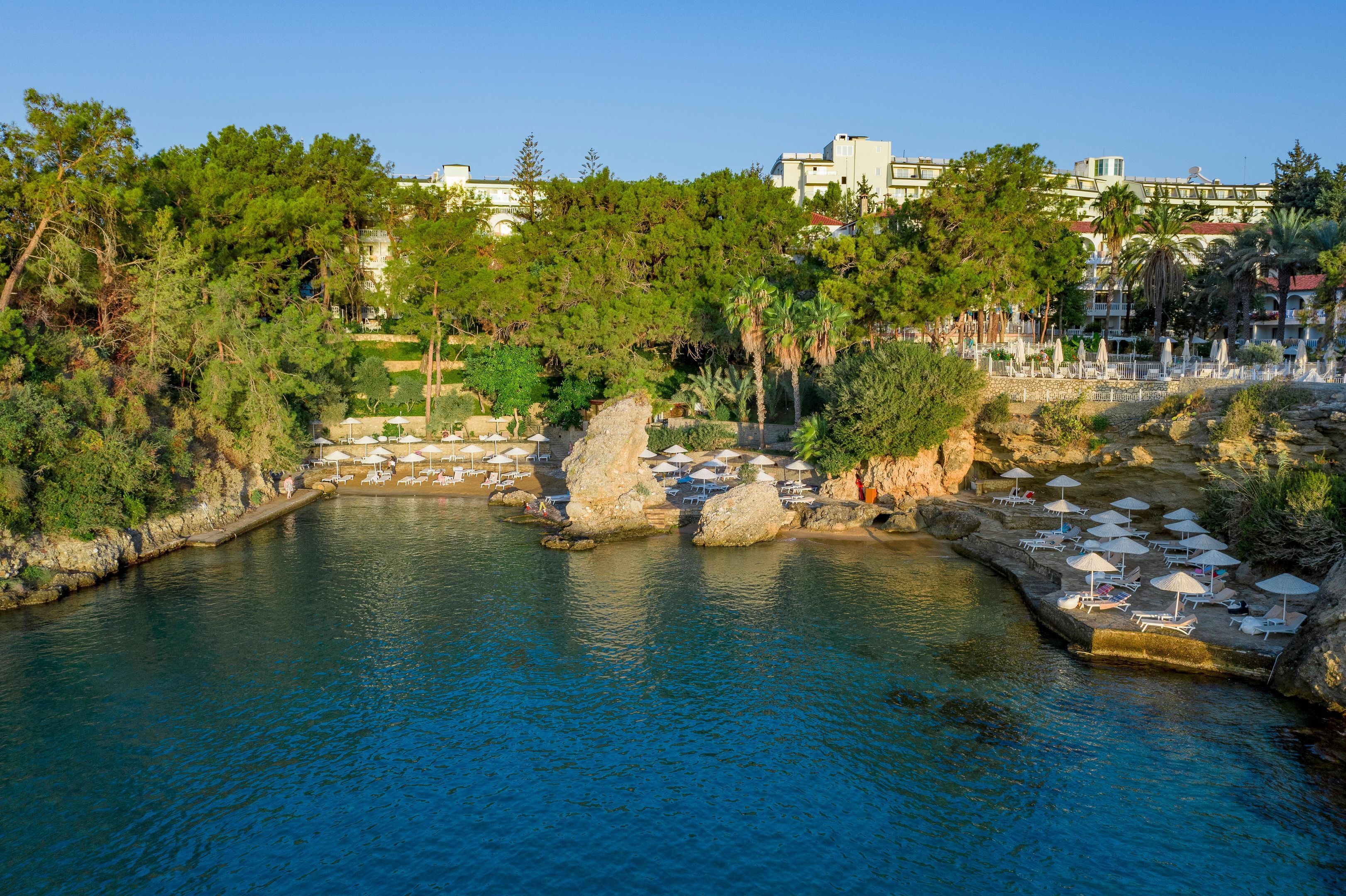 A coastal resort with a rocky shoreline, clear blue water, and a row of sun loungers and umbrellas.