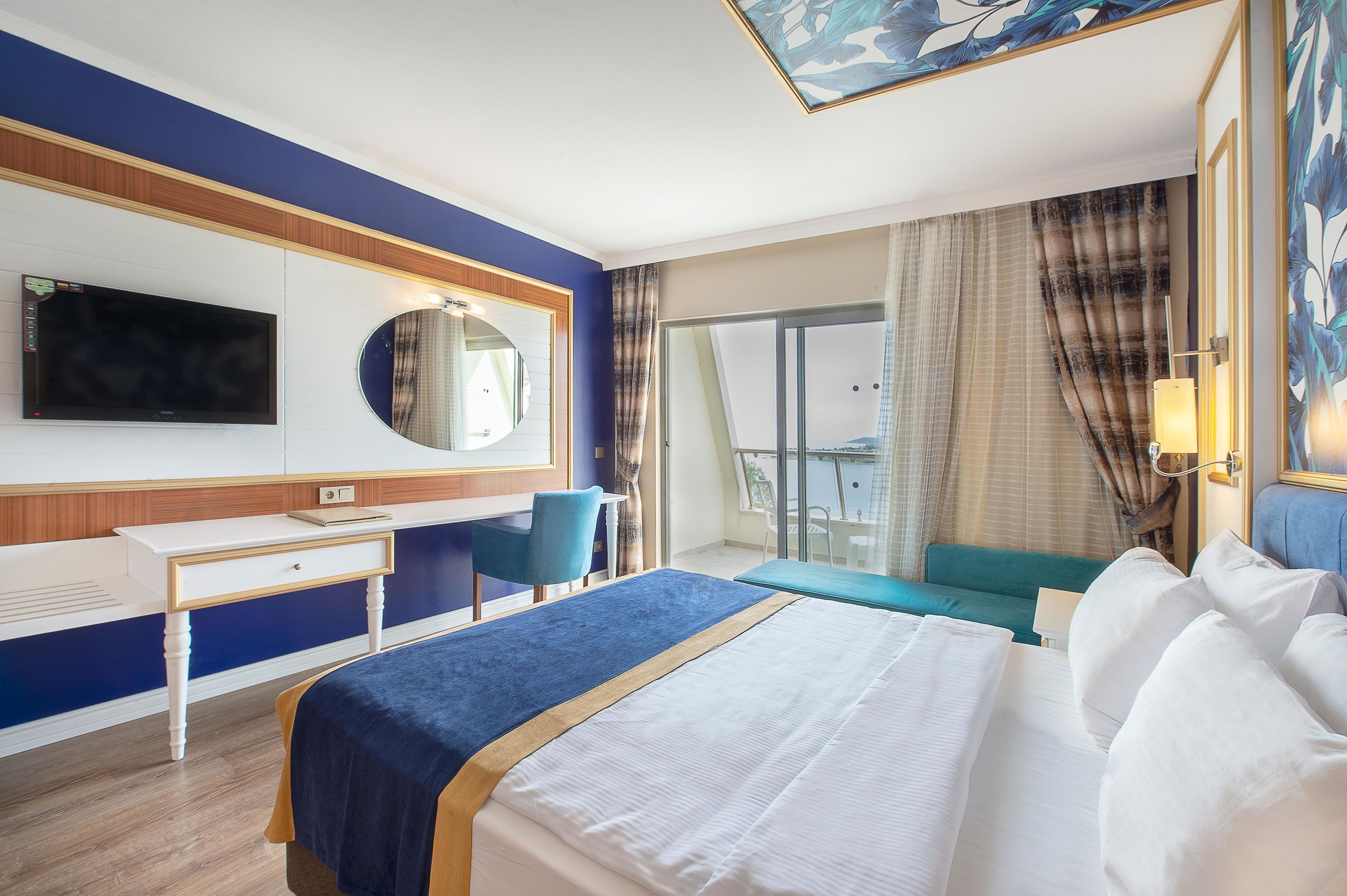 A hotel room with a bed, a desk, a chair, a TV, and a balcony with curtains.