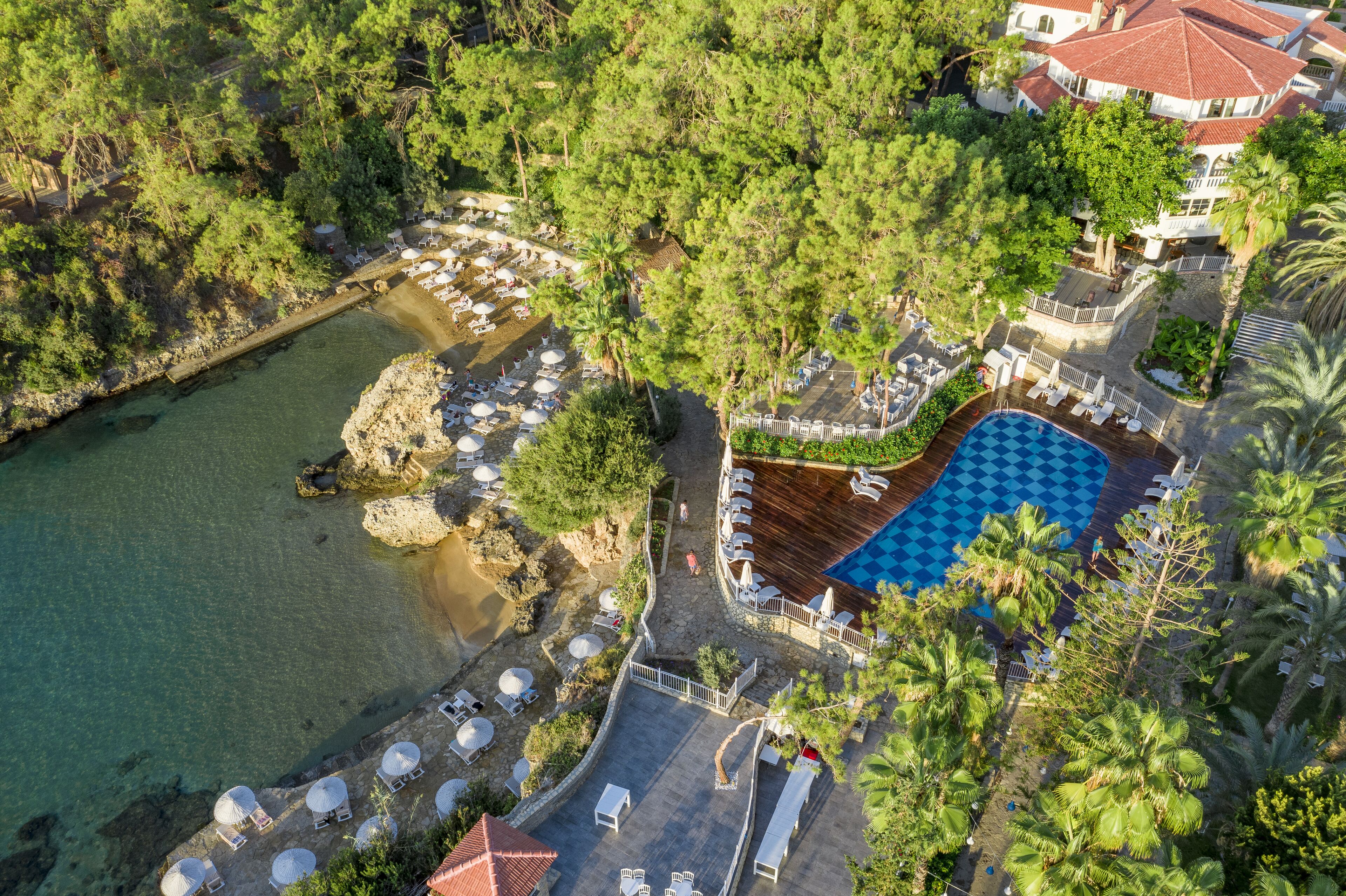 Ett flygbildsfoto av ett semesterområde med en swimmingpool, solstolar och en klippig strand.