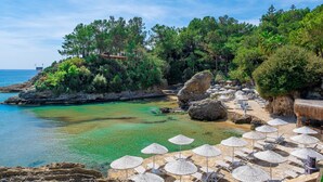 Un complejo turístico en la costa con aguas cristalinas, sombrillas de playa y sillones de descanso.