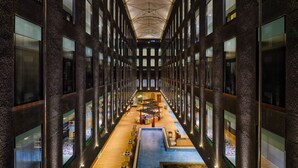 A modern building with a central atrium, multiple floors, and a long corridor with tables and chairs. - Essentia Luxury Hotel Indore (Indore)