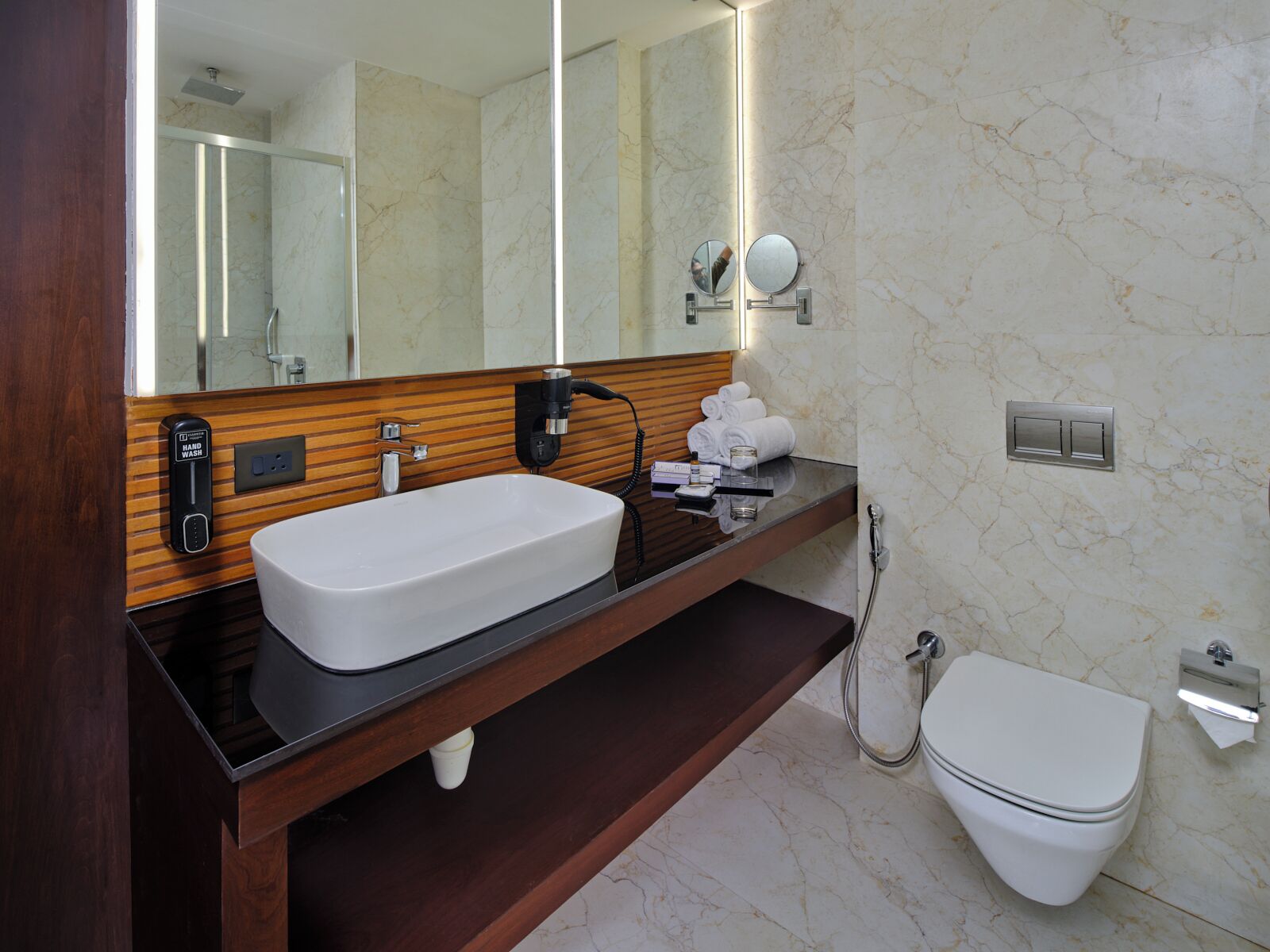 Une salle de bain moderne avec un grand miroir, un lavabo blanc, un meuble-lavabo en bois, des toilettes et une douche.