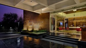 A modern hotel entrance with a stone facade, a reception area with red chairs, and a staircase leading inside. - Essentia Luxury Hotel Indore (Indore)